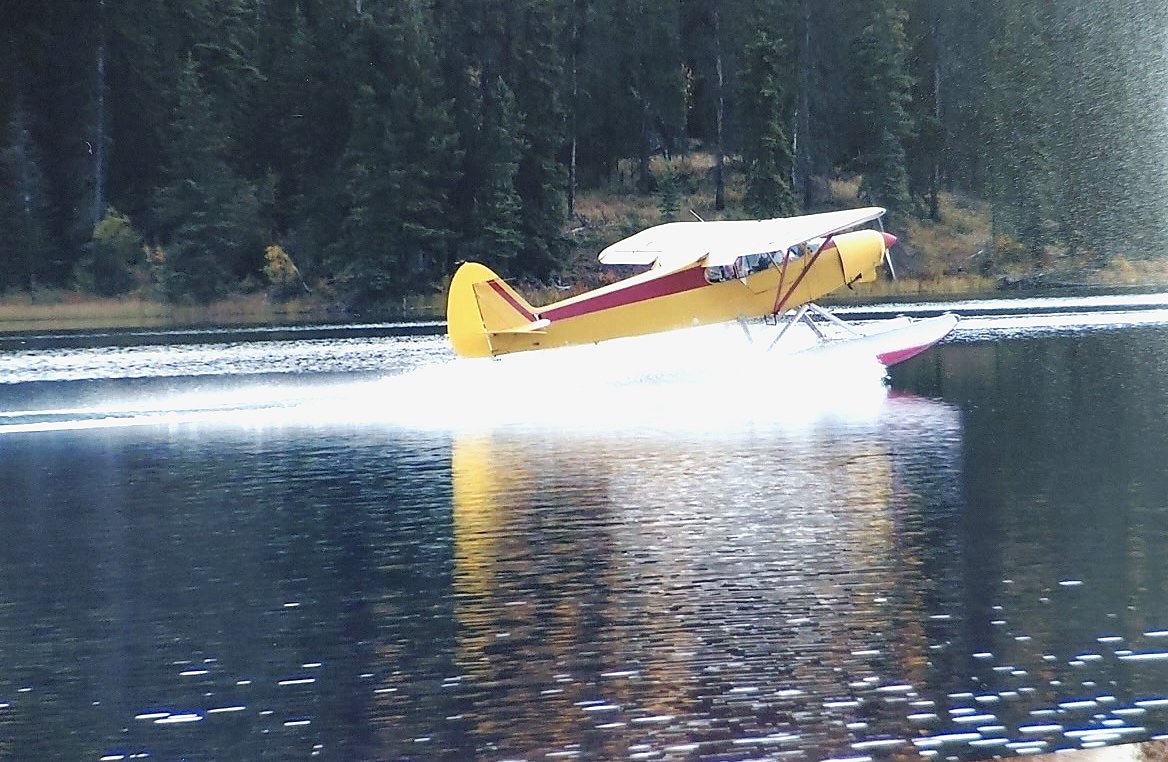A yellow Super Cub on floats lifting off a northern lake.