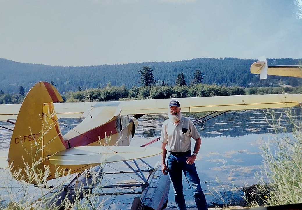 Joe Noble's father standing beside his yellow Super Cub on floats at a lake.
